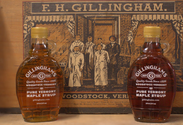 Two bottles of Gillingham's Pure Vermont Maple Syrup in front of a vintage Gillingham's sign.